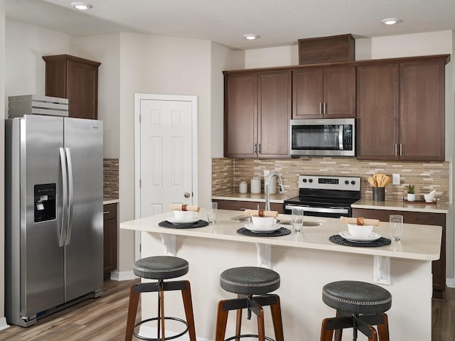 kitchen featuring appliances with stainless steel finishes, hardwood / wood-style floors, an island with sink, sink, and dark brown cabinetry