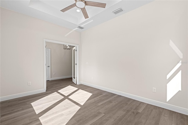 unfurnished room featuring dark hardwood / wood-style flooring, ceiling fan with notable chandelier, and a raised ceiling