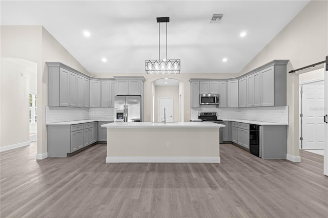 kitchen with pendant lighting, appliances with stainless steel finishes, gray cabinetry, a kitchen island, and a barn door