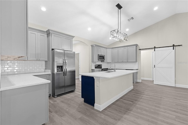 kitchen with vaulted ceiling, appliances with stainless steel finishes, decorative light fixtures, sink, and a barn door