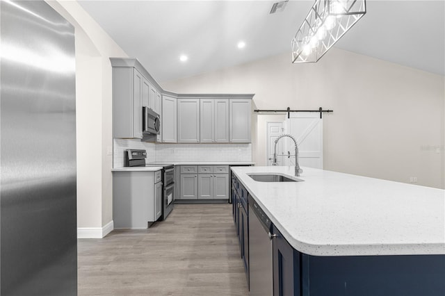 kitchen featuring pendant lighting, sink, appliances with stainless steel finishes, a kitchen island with sink, and a barn door