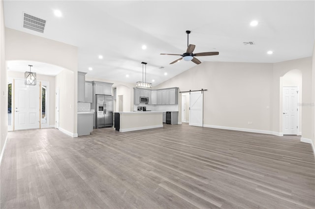 unfurnished living room with wood-type flooring, a barn door, lofted ceiling, and ceiling fan