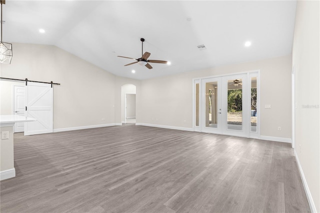 unfurnished living room with hardwood / wood-style flooring, ceiling fan, lofted ceiling, and a barn door