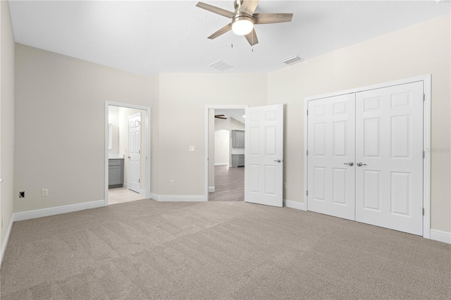 unfurnished bedroom featuring ceiling fan, light carpet, ensuite bath, and a closet