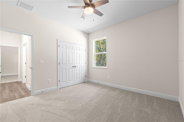 unfurnished bedroom featuring light carpet, ceiling fan, a closet, and a textured ceiling