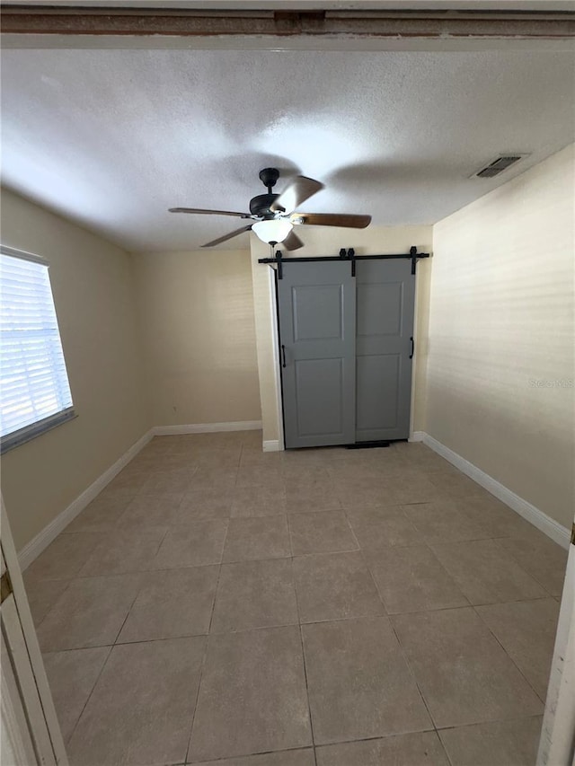 unfurnished room featuring ceiling fan, a barn door, a textured ceiling, and light tile patterned floors