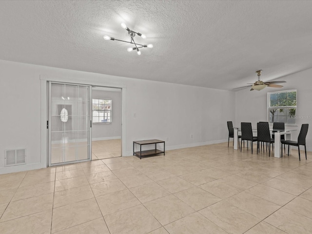 unfurnished room with light tile patterned floors, ceiling fan with notable chandelier, and a textured ceiling