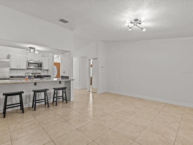 kitchen featuring appliances with stainless steel finishes, lofted ceiling, a breakfast bar area, white cabinets, and kitchen peninsula