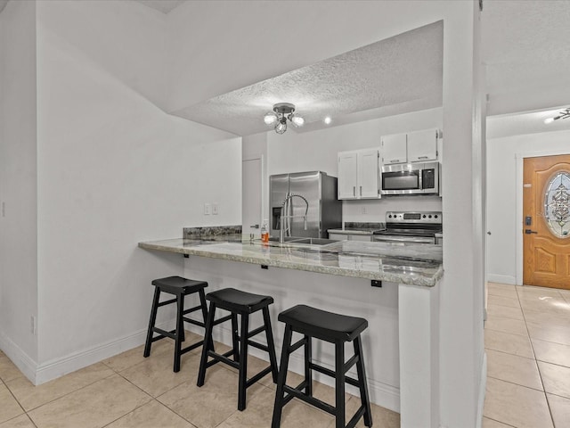 kitchen featuring light stone counters, kitchen peninsula, white cabinets, and appliances with stainless steel finishes