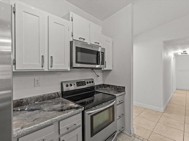 kitchen with white cabinetry, stainless steel appliances, stone countertops, and light tile patterned flooring