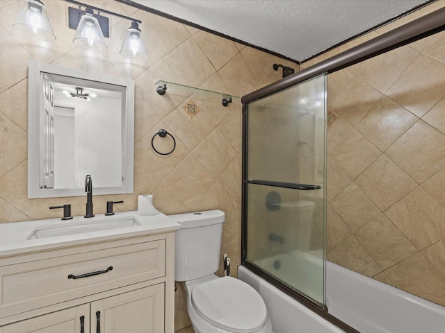 full bathroom featuring tile walls, bath / shower combo with glass door, vanity, a textured ceiling, and toilet