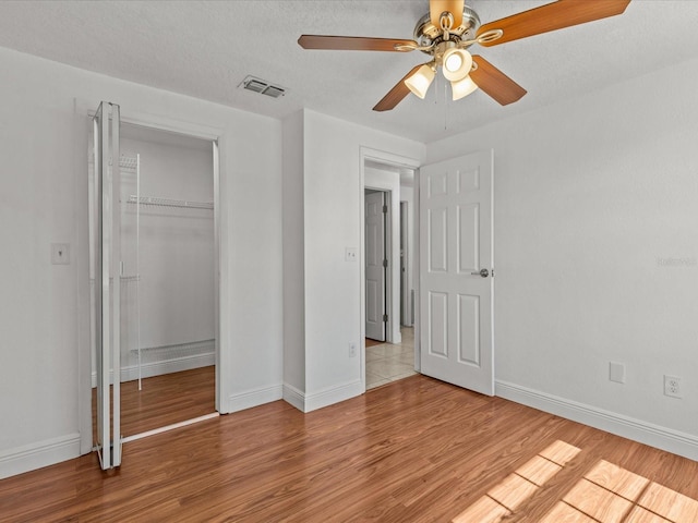 unfurnished bedroom featuring ceiling fan, a textured ceiling, light hardwood / wood-style floors, and a closet