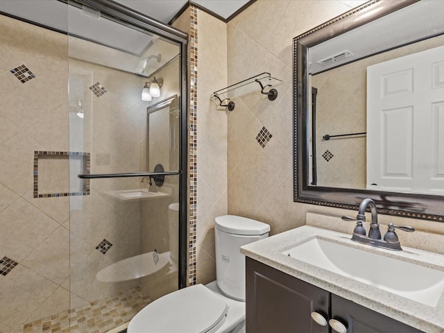 bathroom featuring vanity, a shower with shower door, toilet, and tile walls