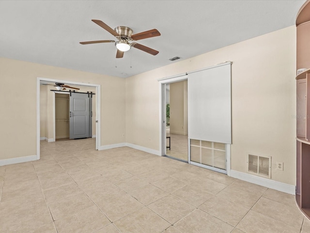 unfurnished bedroom with ceiling fan, a barn door, a closet, and light tile patterned floors