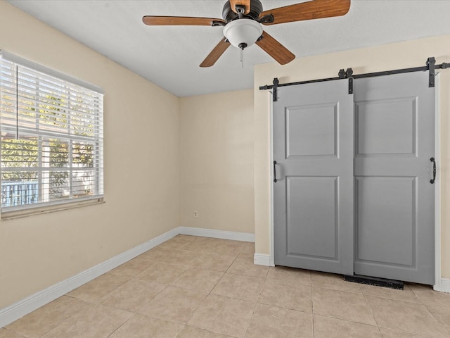 unfurnished bedroom featuring light tile patterned flooring, a barn door, and ceiling fan