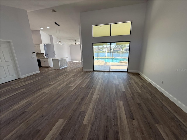 unfurnished living room with sink, dark wood-type flooring, and high vaulted ceiling