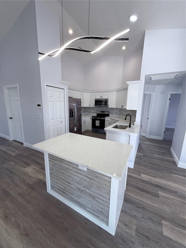 kitchen with sink, appliances with stainless steel finishes, white cabinetry, hanging light fixtures, and high vaulted ceiling