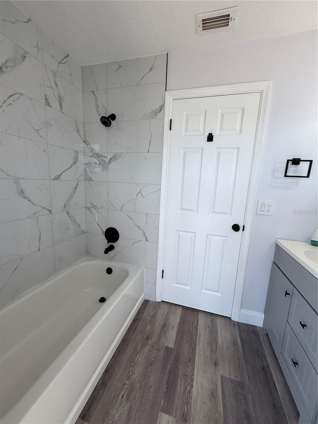 bathroom with vanity, tiled shower / bath combo, hardwood / wood-style floors, and a textured ceiling