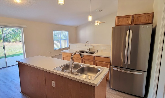 kitchen featuring lofted ceiling, sink, a center island with sink, and stainless steel refrigerator