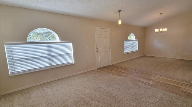 empty room with vaulted ceiling, carpet floors, a textured ceiling, and an inviting chandelier