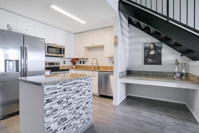 kitchen with stainless steel appliances, light stone countertops, light hardwood / wood-style floors, decorative backsplash, and white cabinets