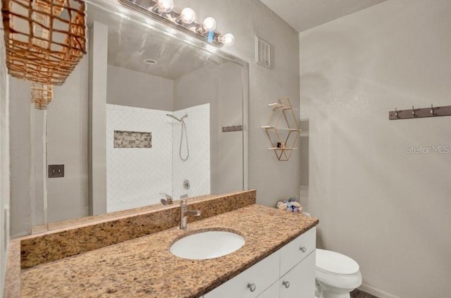 bathroom featuring vanity, a tile shower, and toilet