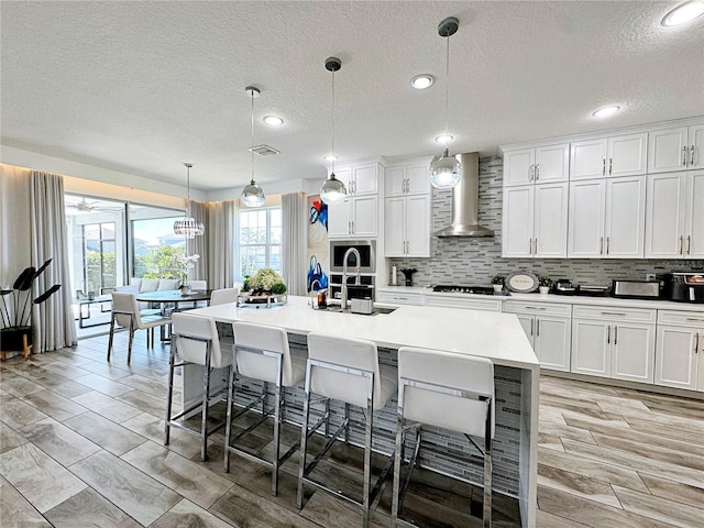 kitchen featuring wall chimney exhaust hood, a breakfast bar, sink, a center island with sink, and pendant lighting