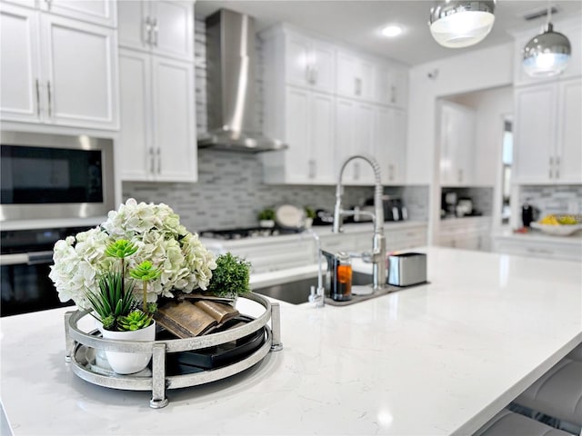 kitchen featuring white cabinets, stainless steel microwave, oven, and wall chimney exhaust hood