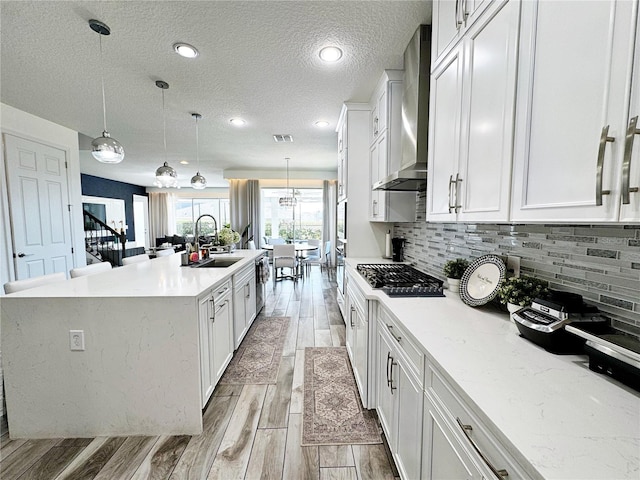 kitchen featuring sink, white cabinets, hanging light fixtures, a center island with sink, and wall chimney exhaust hood