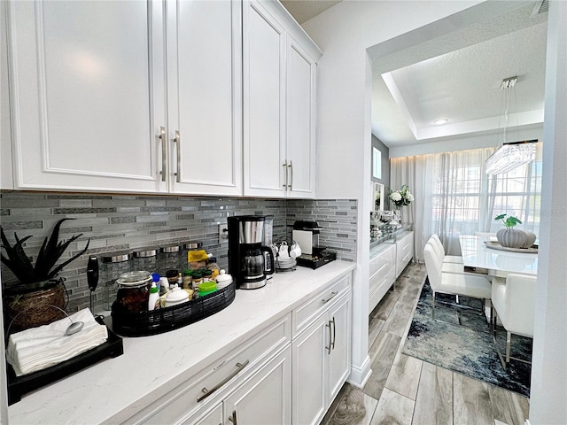 kitchen featuring white cabinetry, light stone counters, a tray ceiling, and backsplash