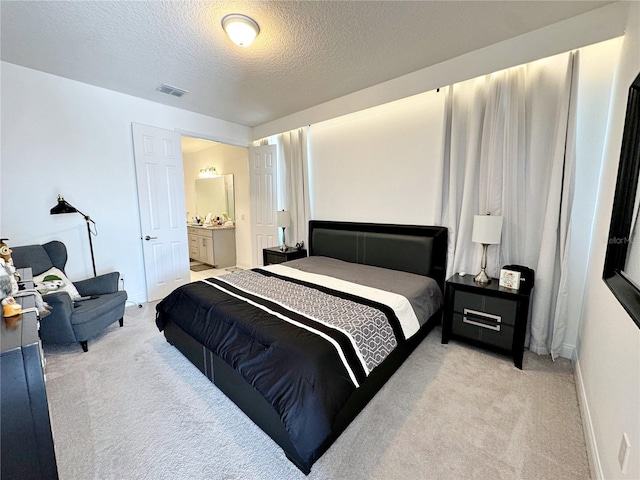 bedroom featuring ensuite bath, light carpet, and a textured ceiling