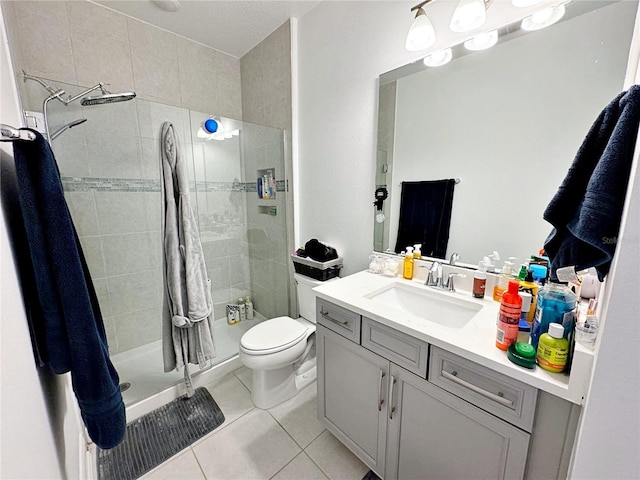 bathroom with tile patterned flooring, vanity, tiled shower, and toilet