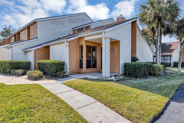 view of front of property featuring stucco siding, a chimney, and a front lawn