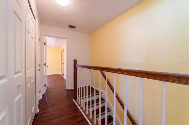 hallway with visible vents, a textured ceiling, dark wood finished floors, and an upstairs landing