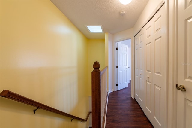 hall featuring dark wood-style flooring, a textured ceiling, and an upstairs landing