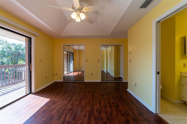 empty room featuring a tray ceiling, visible vents, a textured ceiling, wood finished floors, and baseboards