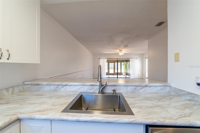 kitchen featuring visible vents, open floor plan, light stone countertops, white cabinetry, and a sink