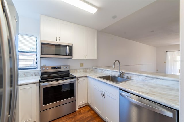 kitchen featuring a peninsula, appliances with stainless steel finishes, a sink, and white cabinets