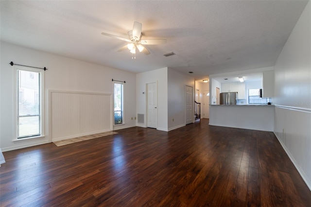 unfurnished living room featuring baseboards, dark wood-type flooring, visible vents, and a ceiling fan