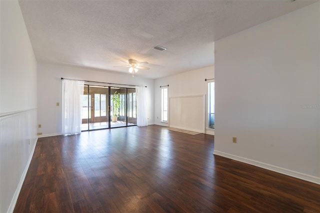 empty room featuring dark wood-style floors, visible vents, a ceiling fan, and a textured ceiling