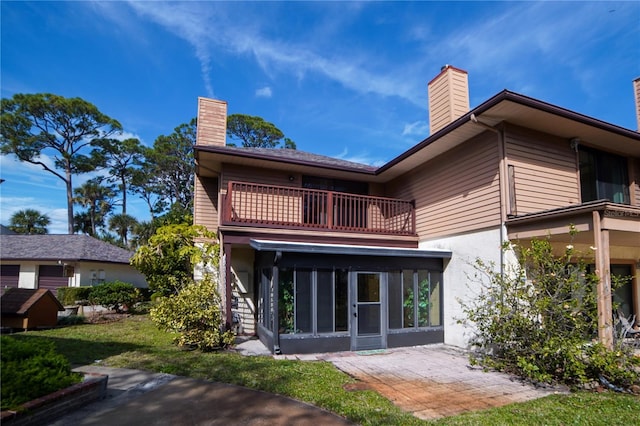 rear view of property with a sunroom, a chimney, a patio area, and a balcony