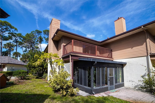 rear view of house featuring a sunroom, a yard, a chimney, and a balcony