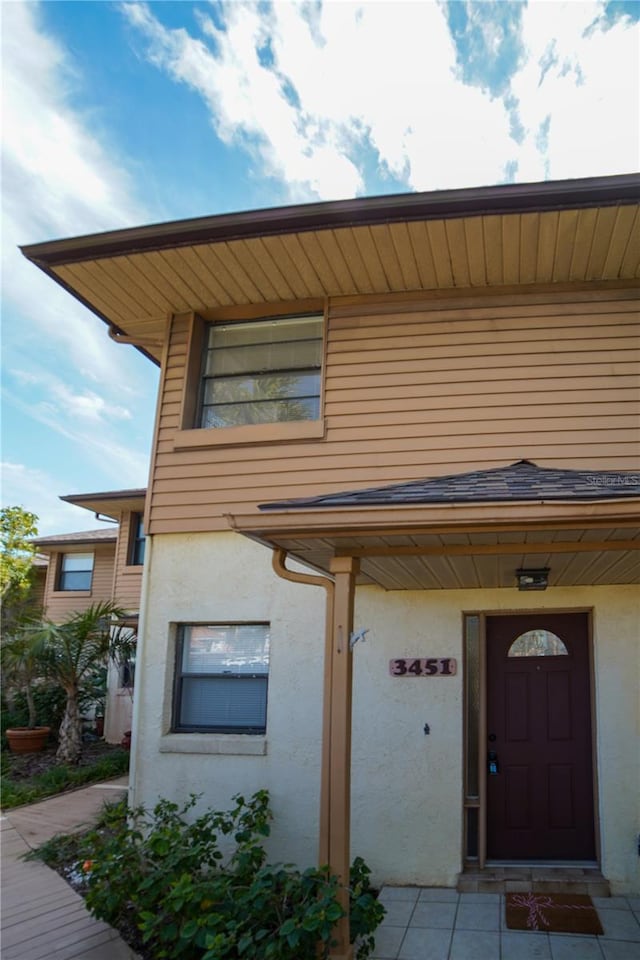 view of exterior entry with roof with shingles and stucco siding