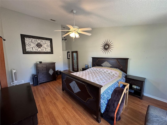 bedroom with lofted ceiling, hardwood / wood-style flooring, a textured ceiling, and ceiling fan