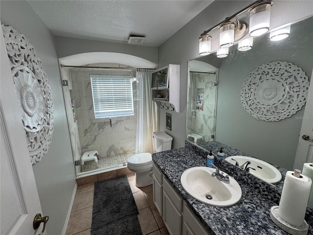 bathroom with tile patterned flooring, vanity, a textured ceiling, a shower with shower door, and toilet