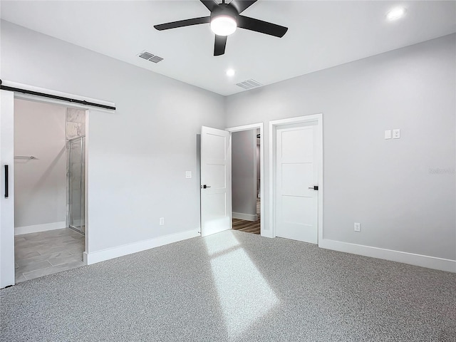 unfurnished bedroom featuring ceiling fan, a barn door, carpet floors, and a spacious closet