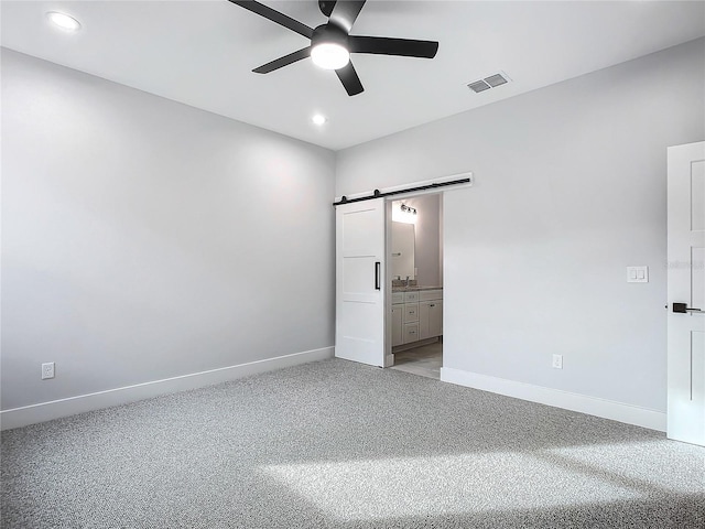 unfurnished bedroom featuring light colored carpet, a barn door, ceiling fan, and ensuite bathroom