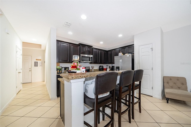 kitchen with appliances with stainless steel finishes, a kitchen breakfast bar, light stone countertops, and light tile patterned floors