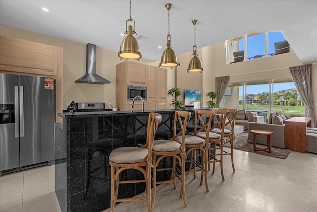 kitchen with appliances with stainless steel finishes, sink, light brown cabinets, hanging light fixtures, and wall chimney range hood