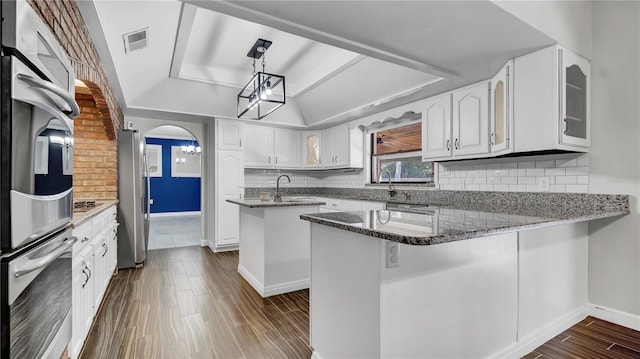 kitchen with stainless steel appliances, kitchen peninsula, white cabinets, decorative light fixtures, and dark stone counters